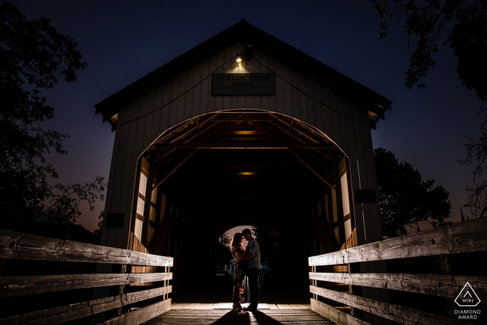 Eagle Point, Oregon, retrato de noivado iluminado à noite | Um casal dentro de uma ponte coberta.