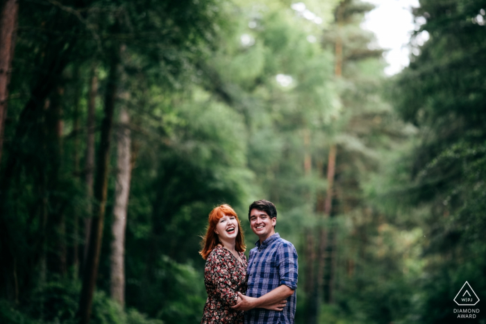 Happy engaged couple laughing during engagement session in the forest trees Irchester Country Park Pre-Wedding Shoot | Happy engaged couple laughing during engagement session