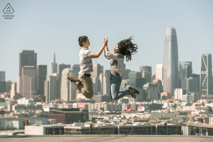 San Francisco, CA tournage de fiançailles avec un couple sautant en l'air, ville en arrière-plan.