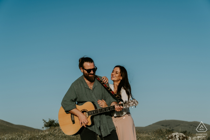 He plays the guitar for her during an engagement shoot under the blue sky Mountains in Abruzzo - Italy | He plays the guitar for her during an engagement shoot under the blue sky