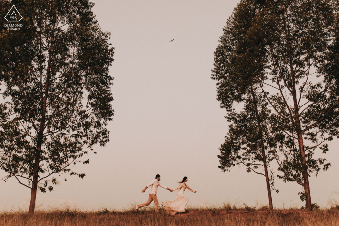 Mateus Leme, Minas Gerais / Brasil couple running in the field between the trees during engagement shoot.