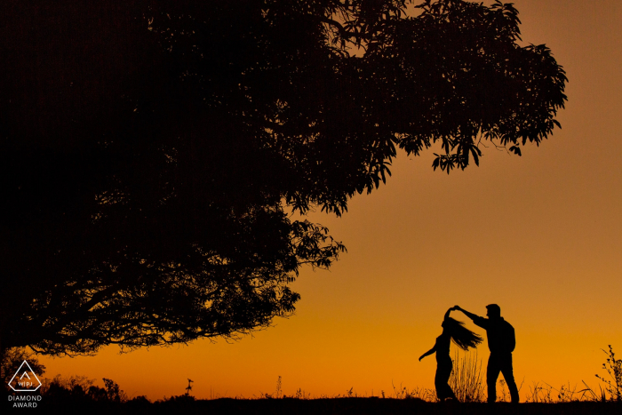 Cedro do Abaeté, Minas Gerais, Brasil | Retratos de silueta de compromiso al atardecer de una pareja girando mientras baila.