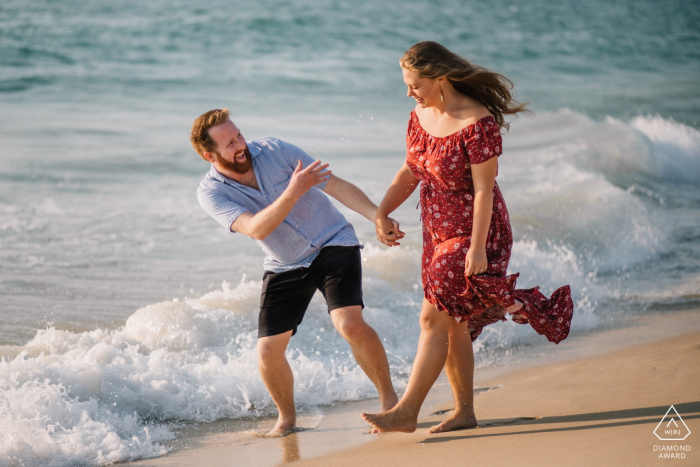 Perth-Paare, die zusammen am Strand während der Verlobungsporträtsitzung gehen und lachen.