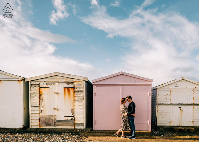 Shoreham Beach, West Sussex, Reino Unido fotografía de compromiso de una pareja abrazada por las cabañas de playa en Shoreham Beach