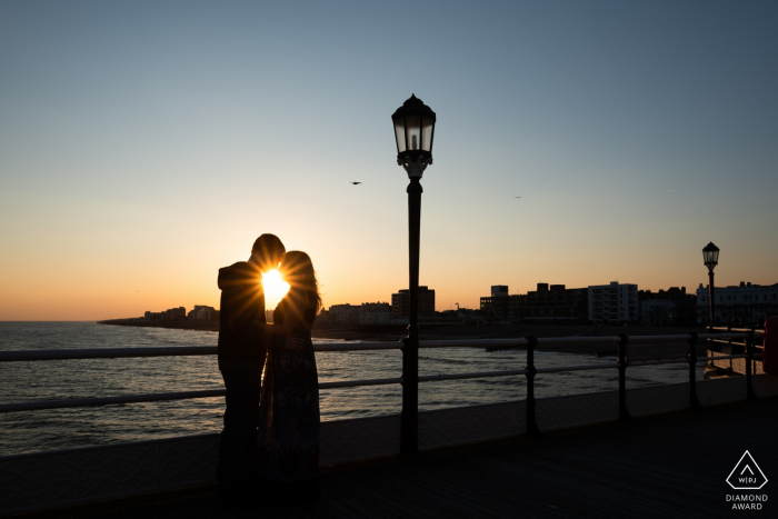 Sul molo di Worthing, Worthing, West Sussex, Regno Unito fotografo di fidanzamento: Silhouette di una coppia con starburst al tramonto sul molo di Worthing