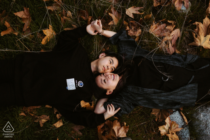 Pasadena, Californie couple allongé dans l'herbe avec des feuilles lors d'une séance photo avant le mariage.