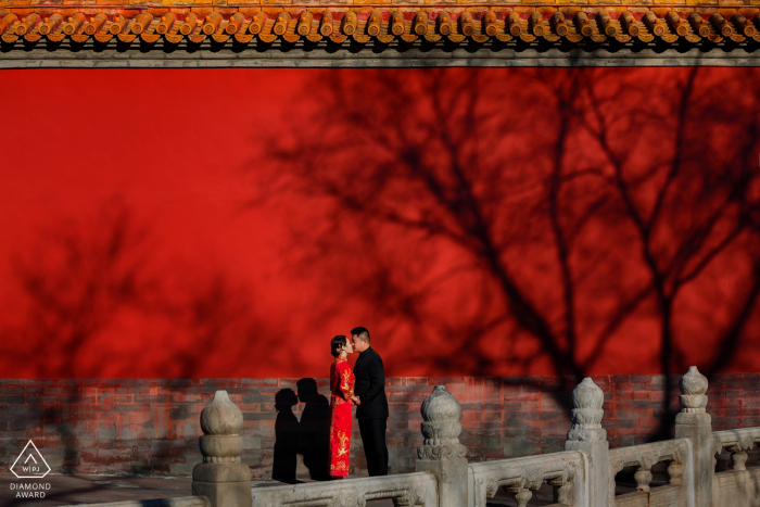 Tiro di foto pre-matrimonio di impegno ardente di amore di Pechino in vestito rosso contro la parete rossa.