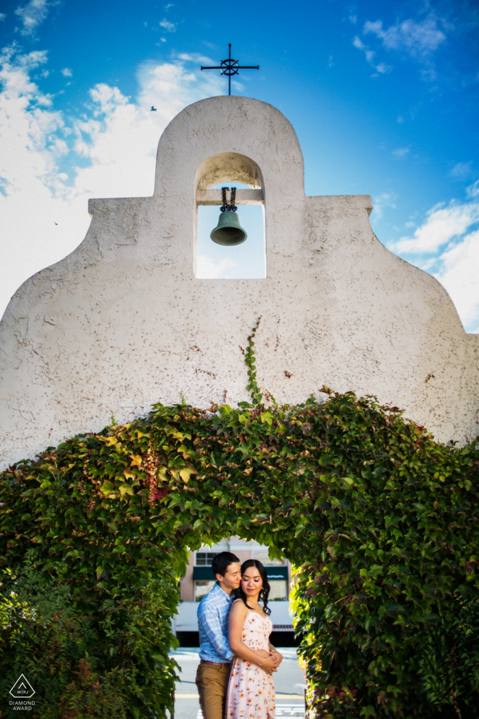 Los Gatos engagement photo shoot of a couple hugging under a mission bell 