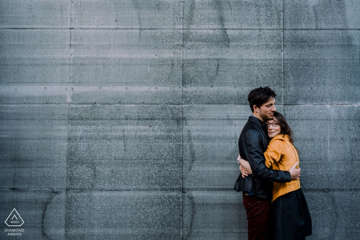 A couple giving a hug in front of a metallic wall in Honfleur, France