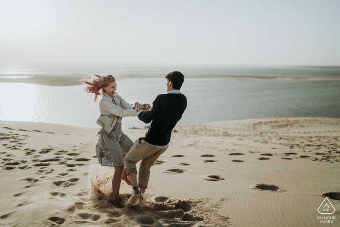 Zdjęcie zaręczynowe Charente-Maritime — tańcząca i wirująca para na piasku plaży.