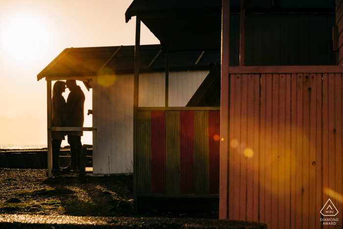 Shoreham Beach, West Sussex, Reino Unido - casal em silhueta emoldurada por cabanas de praia com sunflare