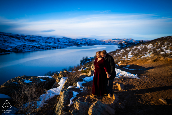 A couple share an intimate moment while trying to stay warm as the sunsets during their winter engagement session at the Reservoir in the foothills A couple share an intimate moment while trying to stay warm as the sunsets during their winter engagement session at Horsetooth Reservoir in the foothills of Fort Collins, Colorado.