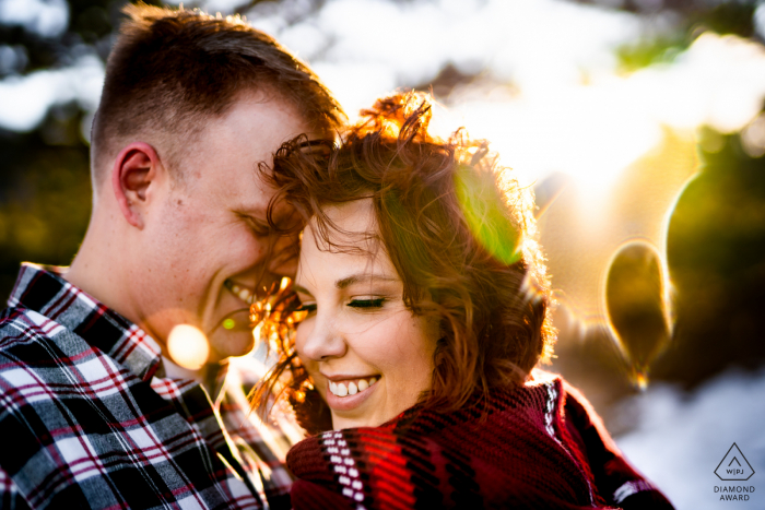 A couple shares an intimate moment while trying to stay warm during their windy winter engagement session at Sprague Lake in Rocky Mountain National Park near Estes Park, Colorado.  