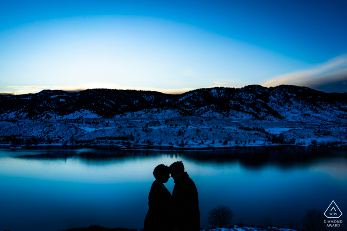 Un couple partage un moment intime tout en essayant de rester au chaud au coucher du soleil lors de leur session de fiançailles hivernale dans les contreforts de Fort Collins, au Colorado.