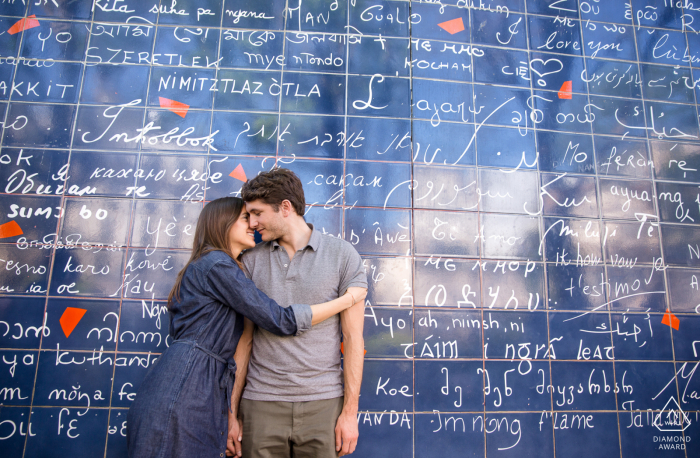 The engaged couple cuddle in front of the wall of love in Paris