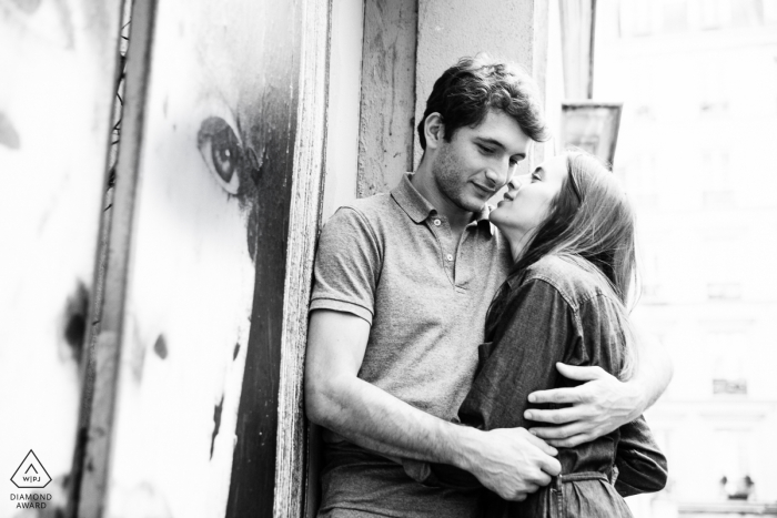 Una pareja de París riéndose frente a un póster gigante para un retrato de compromiso