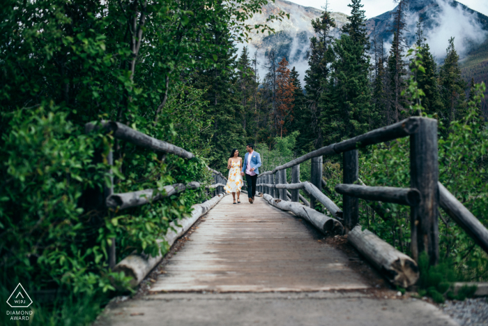 an engaged couple are Running together across a bridge in Pyramid Island, Jasper National Park, AB, Canada	