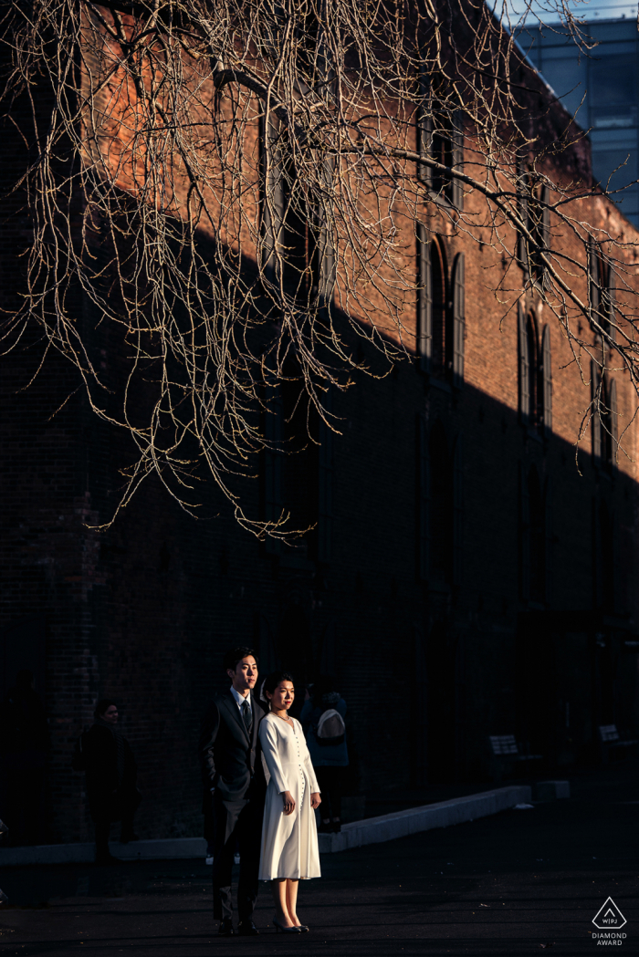 engaged couple in afternoon sunlight near brick building dumbo Portrait of engaged couple in afternoon sunlight
