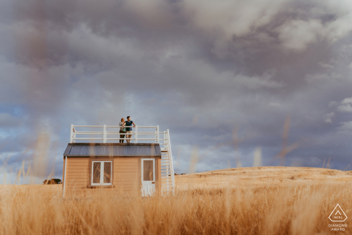 Casal de Godley Head em pé no telhado de uma velha cabana antártica durante a sessão de fotos de noivado de Christchurch na NZ