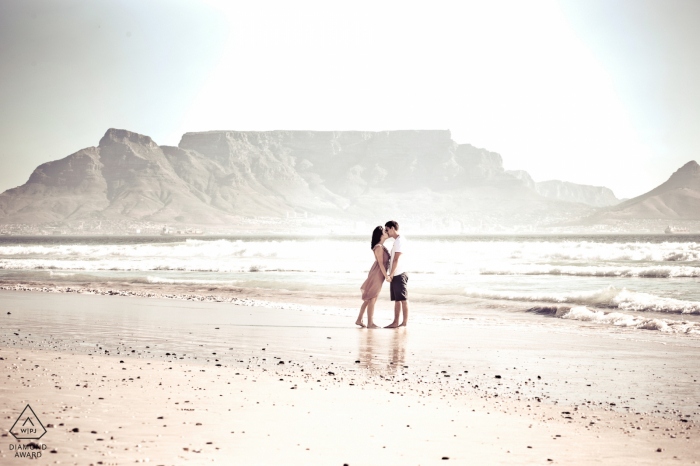 engagement portrait of The couple kissing in front of one of the 7 natural wonders of the world at Blouberg Beach