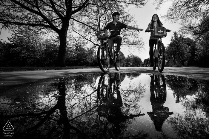 Impegno in bianco e nero in bicicletta della coppia in bicicletta su una riflessione di acqua piovana a Londra, Regno Unito