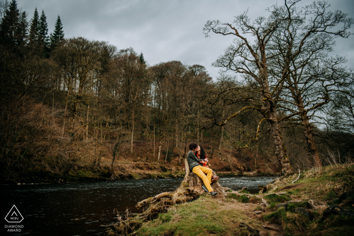 Bolton Abbey, Yorkshire, UK Engagement portrait shoot image montrant le couple s'embrassant alors qu'il était assis sur une souche d'arbre Bolton Abbey, Yorkshire, UK Engagement portrait shoot image montrant le couple s'embrassant alors qu'il était assis sur une souche d'arbre