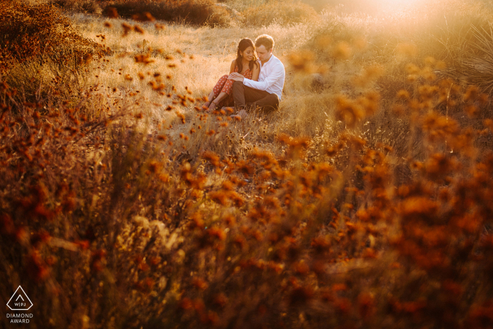 Los Ángeles, California, fotografía previa a la boda de una pareja sentada en un campo abierto en la luz del sol de la tarde