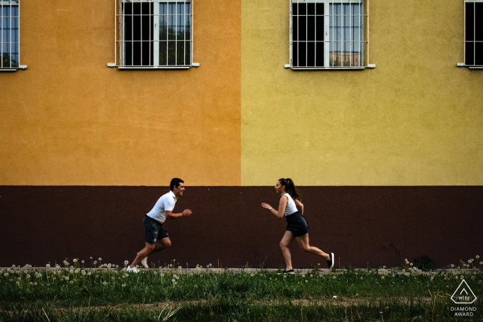 Séance photo avant le mariage à Sofia avec un couple engagé de Bulgarie qui est heureux et joyeux et qui court devant le bâtiment jaune