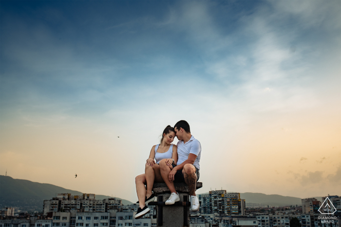 Sessão de retratos antes do casamento na Bulgária com amantes noivos em um telhado de Sofia ao pôr do sol