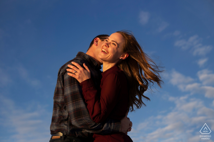 Sessão de fotos de noivado em Alberta no Lago Astonin com um casal rindo com céu azul claro acima