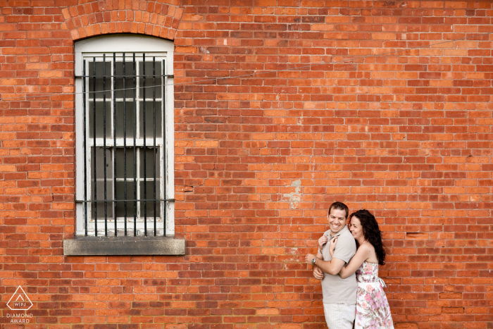 RI engagement photo shoot of a couple in front of brick wall and window iin Newport, Rhode Island