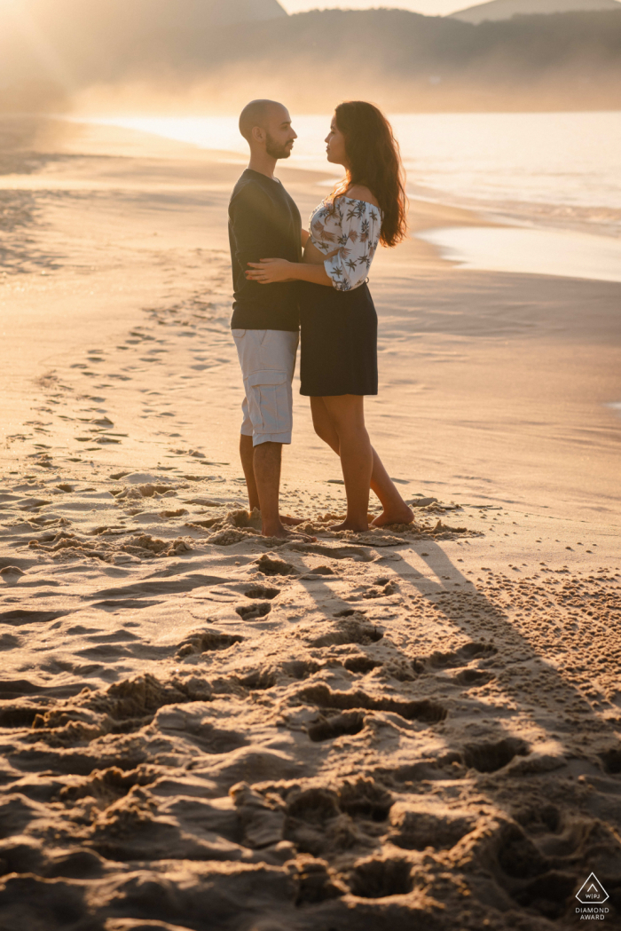 Brazilian engagement portrait with a posed couple standing on the beach sands of Niteroi - RJ Brazil When the sun kisses a backlit image