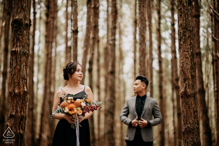 Vietnam forest pre-wedding photo session with an engaged couple holding flowers while standing in the trees of Dalat