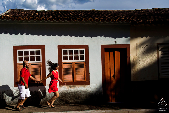 Brazil engagement portrait with a posed couple running through the streets of Cidade de Goiás holding hands in red shirts