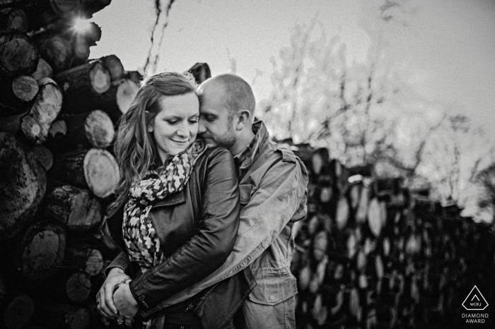 Mini sessão de fotos de casal se abraçando em Hampshire Wood antes do dia do casamento ao lado de lenha cortada e empilhada