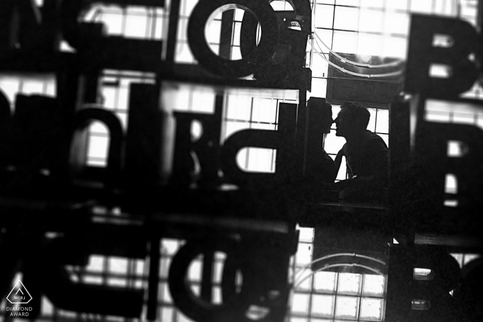 Chicago small indoor photo session with the couple before the wedding day kissing in front of a large pile of architectural sign letters