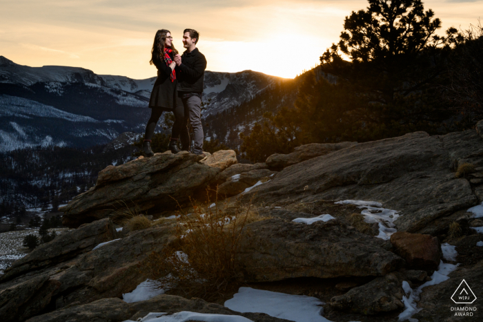 Parque Nacional de las Montañas Rocosas micro sesión de fotos de montaña al aire libre antes del día de la boda con una pareja disfrutando de la puesta de sol en un pico