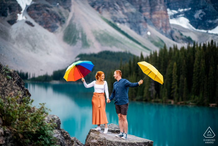 Lago Moraine, Parque Nacional de Banff, AB, Canadá micro sessão de fotos ao ar livre na montanha antes do dia do casamento, no topo de uma rocha com guarda-chuvas coloridos