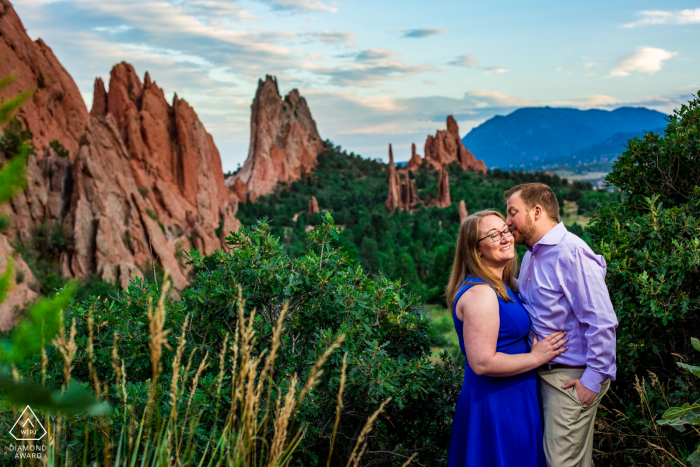 Colorado Springs couple portrait, as he gives his fiancee a smooch on the cheek in front of the incredible summer view of Garden of the Gods.