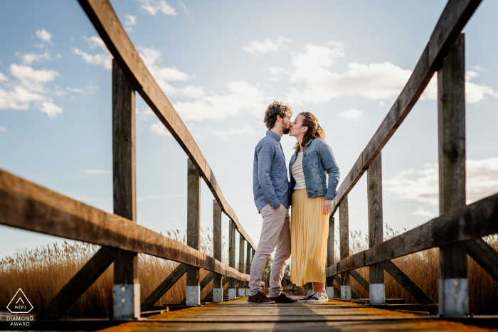 Montpellier, Francia Fine Art Imagen de compromiso de una pareja besándose en un puente peatonal de madera bajo un cielo azul