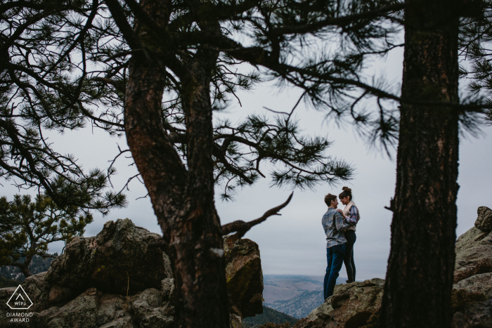 Boulder, CO Fotoshooting vor der Hochzeit im Fine Art Style für ein verlobtes Paar, das sich vor einem Kuss durch silhouettierte Kiefern umarmt