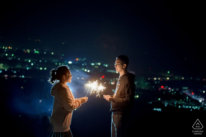 Nanning Fine Art Engagement Session di notte con vista sulle luci della città con una coppia che tiene le stelle filanti