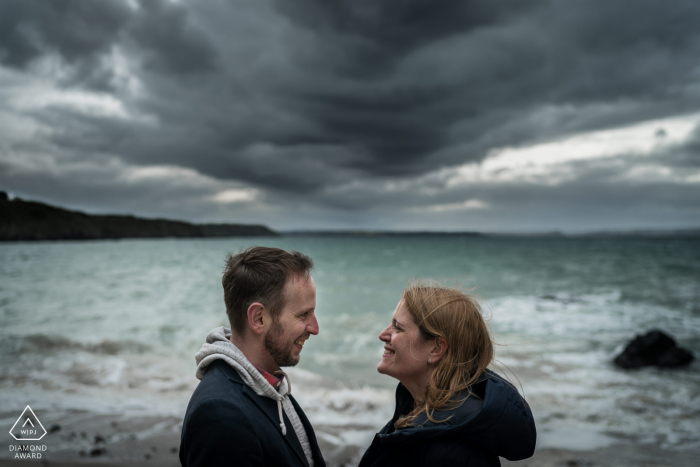 Planguenoual, Frankreich Fine Art Pre Wedding Portrait, niedrig gerahmtes Paar am Strand mit Wolken