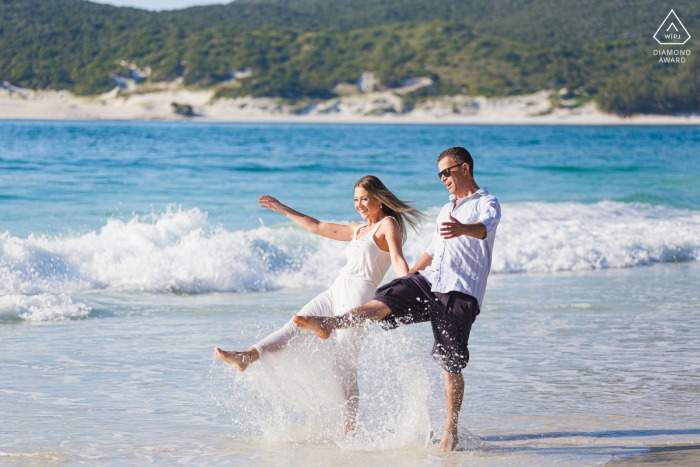 Arraial do Cabo, RJ environmental engagement e-session with the couple kicking up their feet in fun in the shallows by the shore