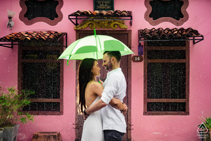 Sesión electrónica de retratos de Phuket con un edificio de color rosa brillante y un paraguas para escapar de la lluvia