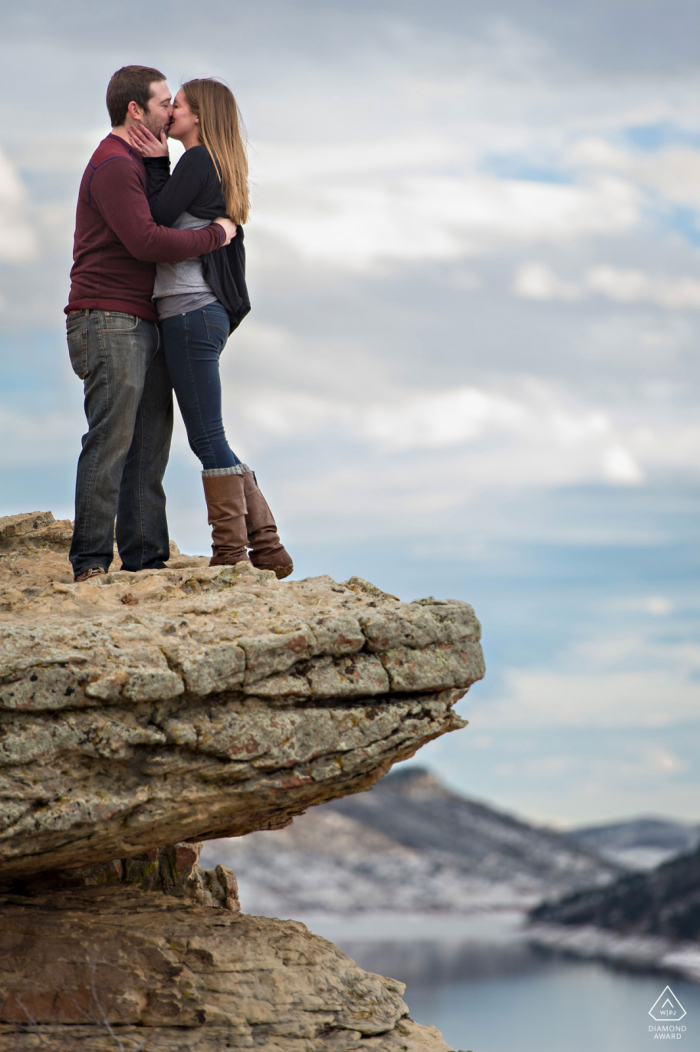 Horsetooth Reservoir, Fort Collins on-location portrait e-shoot of a couple kissing on the rocks overlooking a long reservoir 