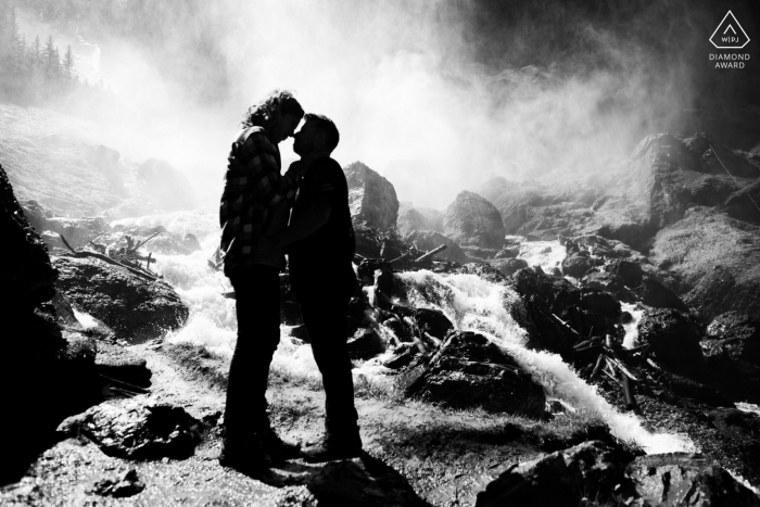 True Love Engagement Posed Portrait in Telluride, das ein Paar einfängt, dem es nichts ausmacht, durchnässt zu werden, als der mächtige Wasserfall sie mit Wasser besprüht