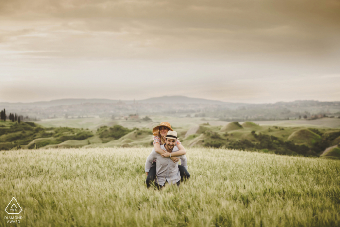 Sessione di ritratti pre-matrimonio di True Love nelle Crete Senesi, Siena che mostra gli amanti della Toscana sulle spalle nella campagna rurale