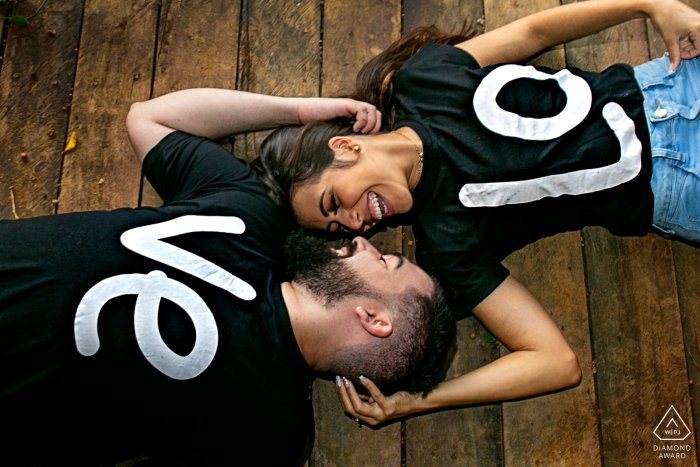 True Love Pre-Wedding Portrait Session at Fazenda Água Limpa in Hidrolândia  illustrating a couple lying on the wooden floor with shirts spelling out L O V E