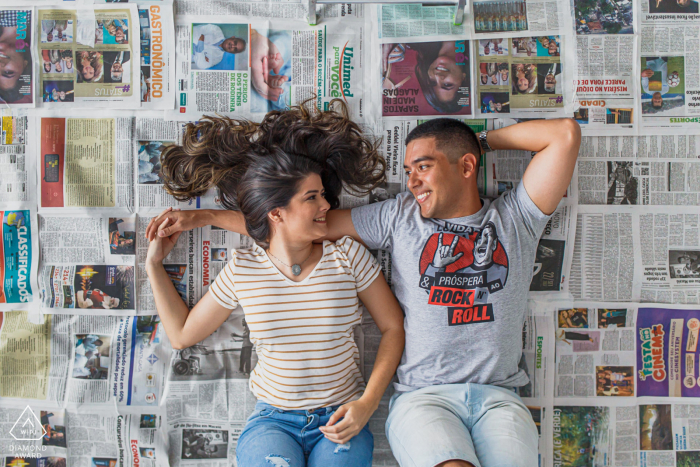 True Love Engagement Portrait Session in Maceió displaying a couple lying down on their backs on a bed of newspapers True Love Engagement Portrait Session in Maceió displaying a couple lying down on their backs on a bed of newspapers